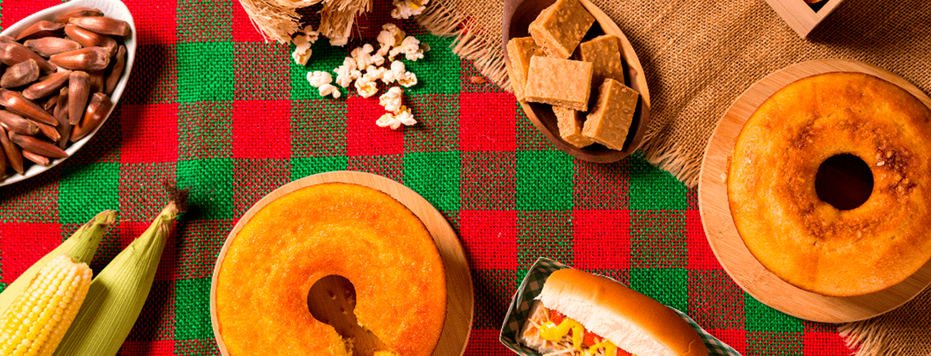 fundo com toalha de mesa xadrez vermelho e verde com bolo fatiado, cachorro quente, pipoca, pé de moleque