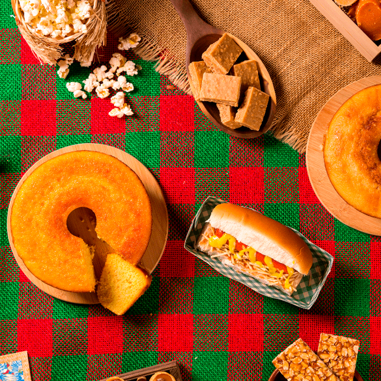 fundo com toalha de mesa xadrez vermelho e verde com bolo fatiado, cachorro quente, pipoca, pé de moleque